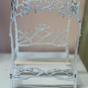 May include: A miniature white bed frame with a delicate, branch-like design. The headboard and footboard feature intricate cut-out patterns of leaves and branches. The bed frame is made of wood and has a light, airy aesthetic, perfect for a dollhouse or miniature setting.