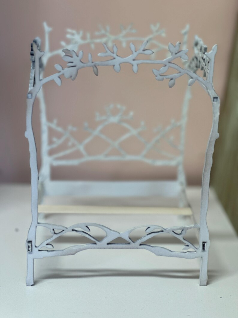 May include: A miniature white bed frame with a delicate, branch-like design. The headboard and footboard feature intricate cut-out patterns of leaves and branches. The bed frame is made of wood and has a light, airy aesthetic, perfect for a dollhouse or miniature setting.