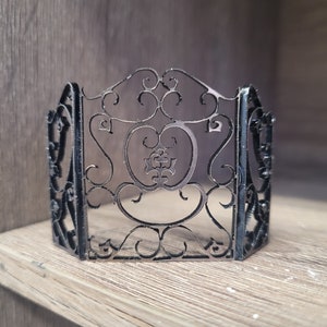 May include: A black metal decorative fireplace screen with a scrolled design. The screen is made of thin metal and has a delicate, intricate pattern.