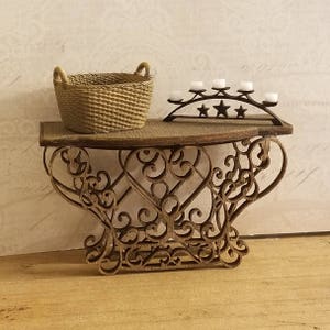 Puede incluir: Una mesa de madera con una base de metal decorativa y con volutas. La mesa tiene una cesta tejida y un candelero de metal con cinco velas en la parte superior.