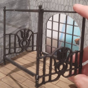 Puede incluir: Un marco de cama con dosel de metal negro con intrincados detalles de volutas. El marco est&aacute; hecho de finas barras de metal y tiene un dise&ntilde;o decorativo.