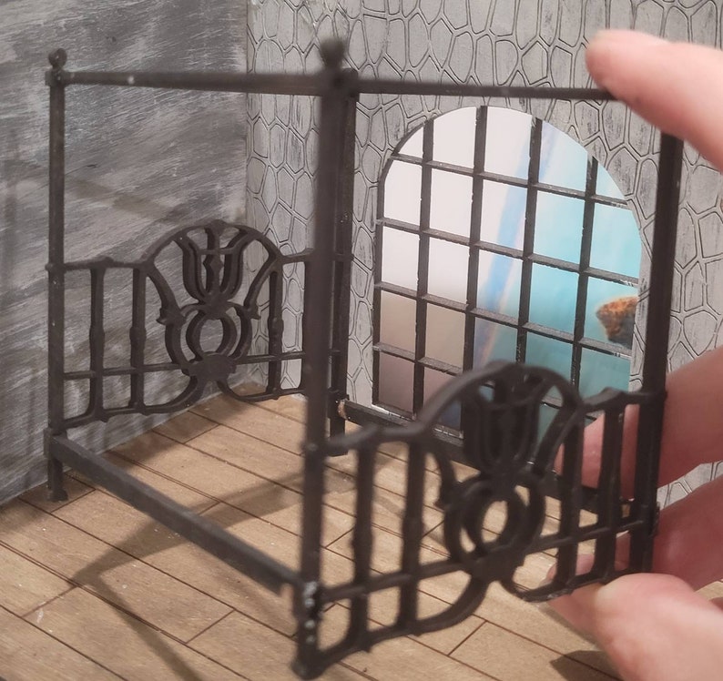 Puede incluir: Un marco de cama con dosel de metal negro con intrincados detalles de volutas. El marco est&aacute; hecho de finas barras de metal y tiene un dise&ntilde;o decorativo.