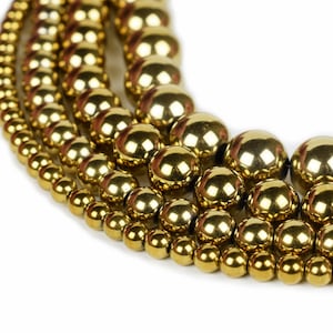 May include: A close-up of a multi-strand necklace made of shiny gold beads. The beads are arranged in a circular pattern, creating a layered effect.