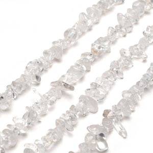 May include: A strand of clear quartz crystal chips, also known as rock crystal, arranged in a row. The chips are irregular in shape and size, with some having a pointed or jagged edge. The chips are strung together on a clear thread.