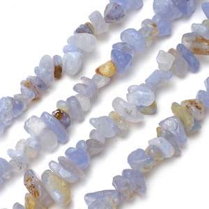 May include: Close-up of strands of blue lace agate chip beads. The beads are a mix of pale blue, white, and yellow-brown colors. The chips are irregular in shape and size, creating a natural, organic look. Ideal for jewelry making.