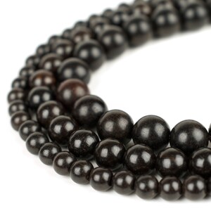 May include: A close-up of a black wooden bead necklace. The beads are arranged in a circular pattern, with the largest beads in the center and the smallest beads on the outside.