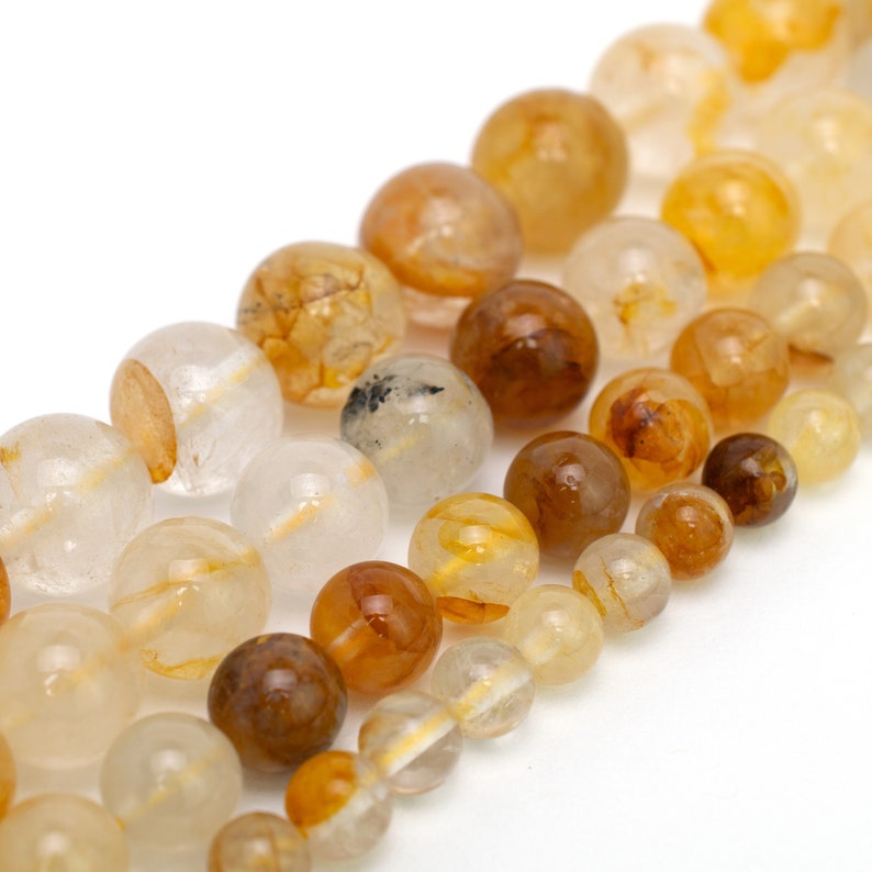 May include: A strand of round, translucent beads with shades of clear, white, and amber. The beads have a natural, organic look with inclusions of golden and brown hues.