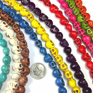 Puede incluir: Una variedad de cuentas de calavera de colores, incluyendo turquesa, blanco, marr&oacute;n, amarillo, azul, morado, rojo, rosa y verde. Las cuentas est&aacute;n dispuestas en filas y tienen aproximadamente el tama&ntilde;o de una moneda de diez c&eacute;ntimos de euro.