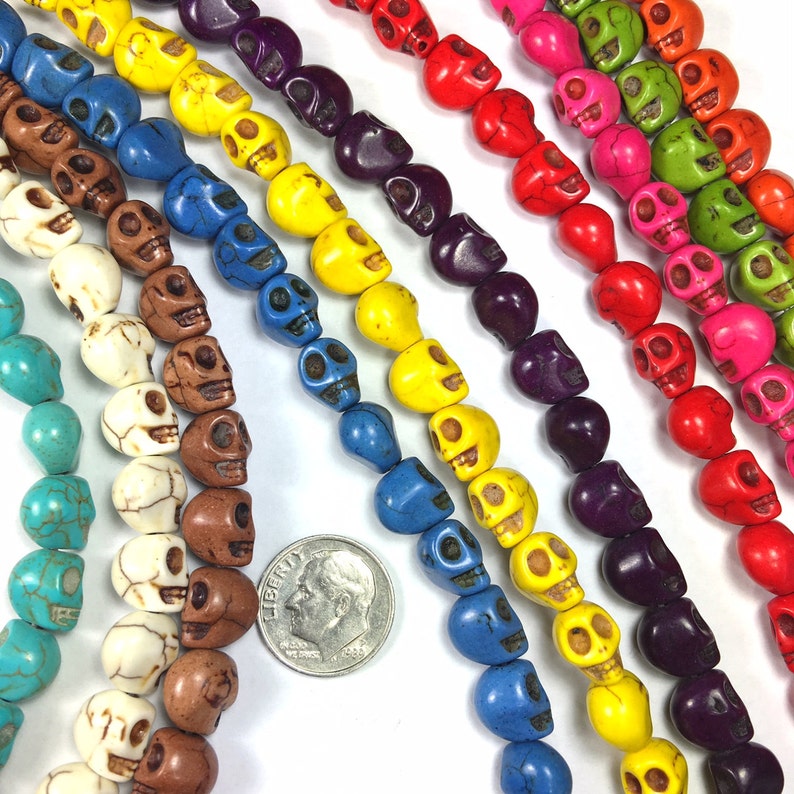 Puede incluir: Una variedad de cuentas de calavera de colores, incluyendo turquesa, blanco, marr&oacute;n, amarillo, azul, morado, rojo, rosa y verde. Las cuentas est&aacute;n dispuestas en filas y tienen aproximadamente el tama&ntilde;o de una moneda de diez c&eacute;ntimos de euro.