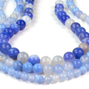 May include: A strand of blue agate beads in various shades of blue, from light to dark, with white striations. The beads are round and smooth, and they are strung on a clear thread.
