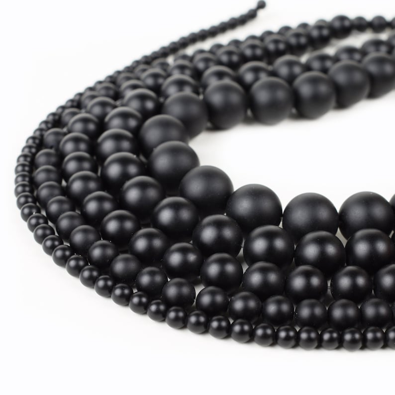 May include: A collection of black matte round beads of various sizes. The beads are arranged in a circular pattern, creating a visually appealing display.