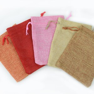 May include: Five small drawstring bags made of burlap fabric in various colors, including orange, red, pink, beige, and brown.