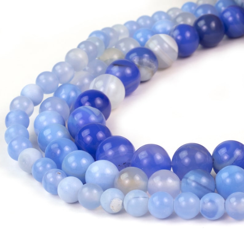 May include: A strand of blue agate beads in various shades of blue, from light to dark, arranged in a graduated pattern. The beads are round and smooth, with a polished finish.