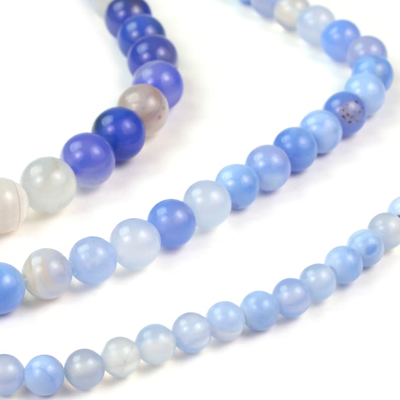 May include: A strand of blue agate beads with a gradient of color from light to dark blue. The beads are round and smooth.