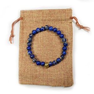 May include: A blue and gold beaded bracelet with a gold charm, in a brown burlap drawstring bag.