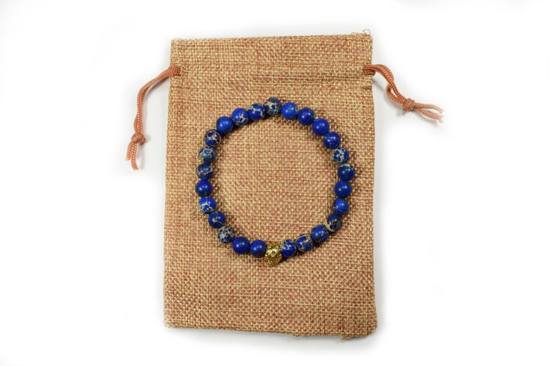 May include: A blue and gold beaded bracelet with a gold charm, in a brown burlap drawstring bag.