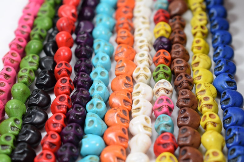 Puede incluir: Primer plano de una variedad de cuentas de calavera de colores. Las cuentas est&aacute;n hechas de turquesa, rojo, naranja, blanco, amarillo, marr&oacute;n, verde, negro y azul.