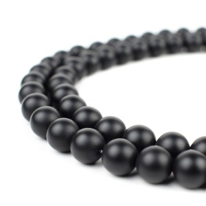May include: A strand of black matte round beads, arranged in a circle on a white background.