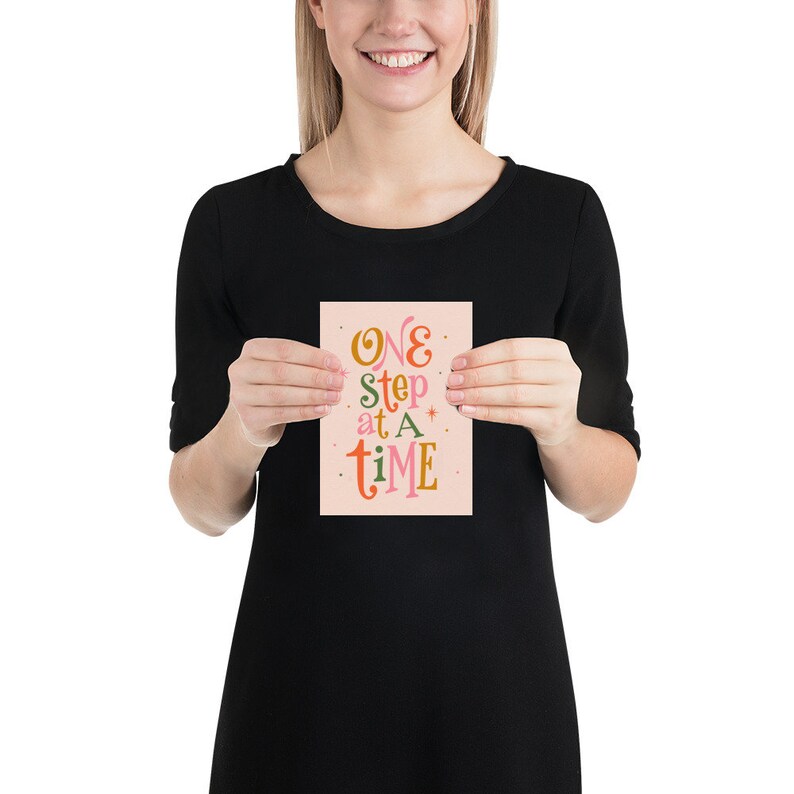 May include: A pink card with the text "ONE step at a time" in colorful, stylized lettering.