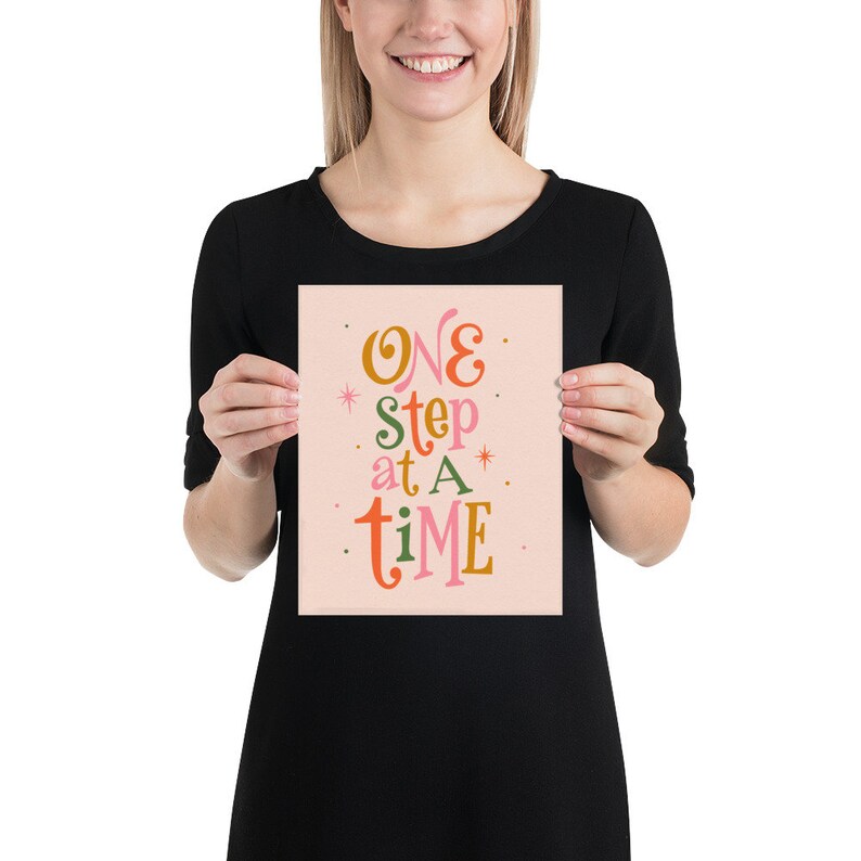 May include: A pink poster with the text "ONE step at A time" in colorful, stylized lettering.