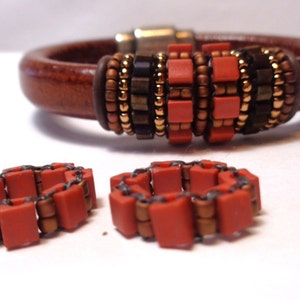 May include: A brown leather bracelet with a beaded design featuring orange, brown, and gold beads. Two smaller beaded rings are also shown.