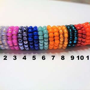 May include: Twelve rows of colorful seed beads, each row numbered 1 through 12. The beads are arranged in a rainbow pattern, starting with green and ending with green.