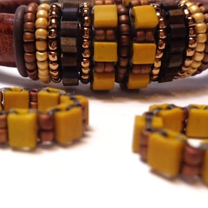 May include: A set of three bracelets made with brown leather, gold, and yellow beads. The bracelets are stacked on top of each other.