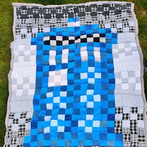 May include: A blue and white patchwork quilt with a large blue square in the centre. The quilt is made of different fabrics, including denim and plaid.