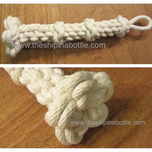 May include: A handcrafted, off-white rope dog toy with multiple knots and a loop at one end. The text "theshipinabottle.com" is visible on the toy. The toy is made of thick, woven rope.