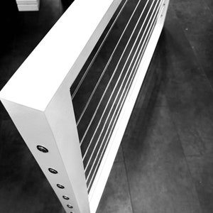 May include: A white frame with a grid of silver wires. The frame is mounted on a wall and has a series of small silver buttons along the side.