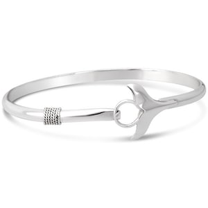 May include: A silver bangle bracelet with a whale tail clasp. The bracelet has a smooth, polished finish and a decorative rope-like detail near the clasp. The whale tail clasp is a prominent feature, adding a nautical touch to the jewelry.