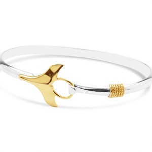 May include: A silver bangle bracelet with a gold whale tail charm and a gold accent on the band.