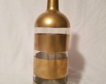 May include: A gold glass bottle with clear glass bands around the bottle. The bottle is painted gold with a matte finish.