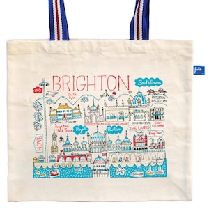 May include: Cream-colored tote bag featuring a colorful illustrated map of Brighton, England, with landmarks and the word "BRIGHTON" in red. The bag has blue handles with red and white stripes.