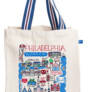 May include: Cream-colored tote bag featuring a colorful map of Philadelphia landmarks, including the Liberty Bell and City Hall. The bag has blue and white striped handles and the word "PHILADELPHIA" in large letters.