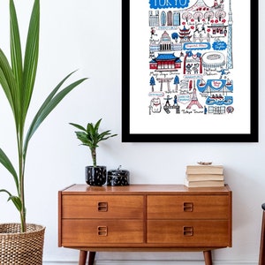 May include: A framed art print featuring a hand-drawn map of Tokyo, Japan. The illustration includes iconic landmarks like Tokyo Tower, Shibuya Crossing, and Meiji Jingu Shrine, rendered in blue, red, and black ink on a white background.