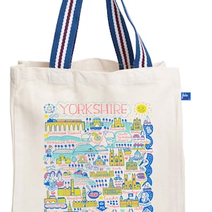 Puede incluir: Bolso tote color crema con un mapa ilustrado colorido de Yorkshire, Inglaterra. El mapa incluye puntos de referencia y la palabra "YORKSHIRE" en rosa. El bolso tiene asas a rayas azules y blancas.