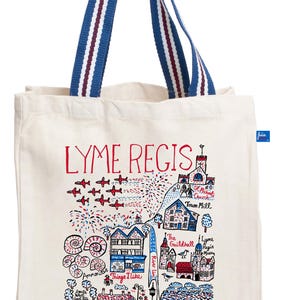 May include: Cream-colored tote bag with a colorful illustration of Lyme Regis, featuring buildings, landmarks, and the text "LYME REGIS." The bag has blue and red striped handles.