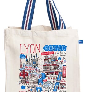 May include: A cream-coloured tote bag with a colourful illustrated map of Lyon, France. The bag features blue and white striped handles. The map includes landmarks and text such as "LYON", "Rhone-Alpes", and "Vieux Lyon".