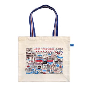 Puede incluir: Bolso tote de color crema con asa a rayas azules y blancas. El bolso presenta una colorida ilustración de los lugares emblemáticos de West Yorkshire y el texto "WEST YORKSHIRE" en rojo. Una pequeña etiqueta azul está adjunta al lateral.