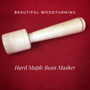 May include: A wooden bean masher made from hard maple with a black accent line.  "Beautiful Woodturning" and "Hard Maple Bean Masher" are written in white text on a red background.
