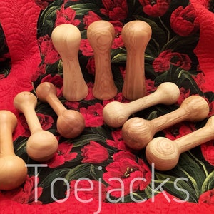 May include: A set of wooden toy jacks, with a variety of shapes and sizes. The jacks are made of natural wood and have a smooth finish. The jacks are arranged on a red and black floral fabric.