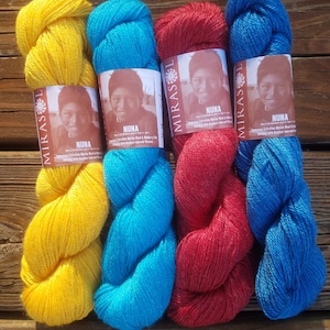 May include: Four skeins of colorful yarn in yellow, turquoise, red, and blue. Each skein has a label with a portrait and the word "NUNA". The yarn is arranged on a wooden surface, showcasing the vibrant colors and textures of the fiber.
