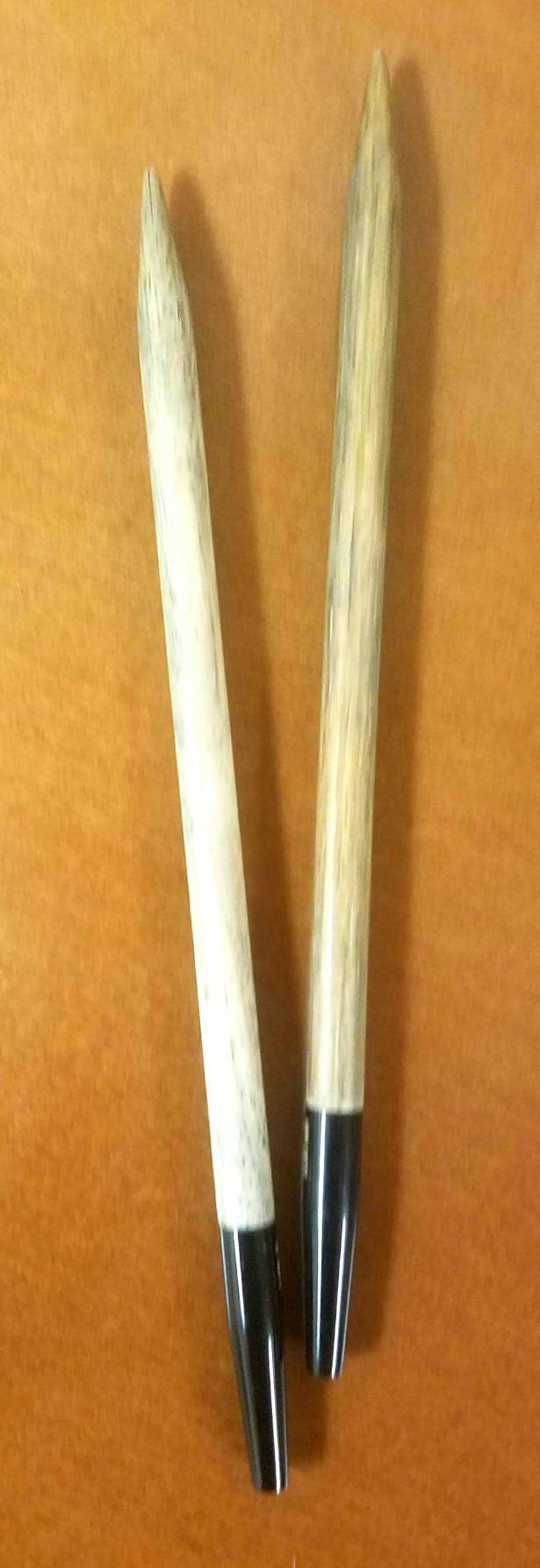 May include: Two wooden knitting needles with black tips. The needles are approximately 12 inches long.