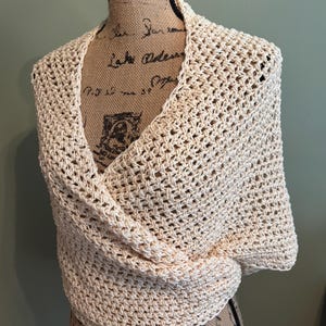 May include: A crocheted shawl in a cream color. The shawl is made with a simple stitch pattern and has a delicate, openwork design.