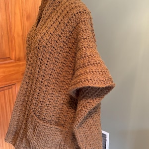 May include: A brown crocheted cardigan with a shawl collar and a pocket on the front.