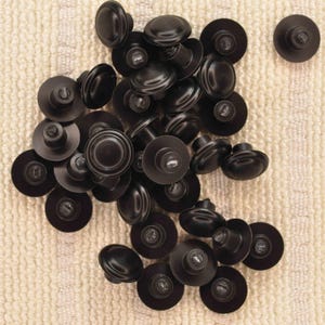May include: A collection of black cabinet knobs with a rounded top and a circular base. The knobs are scattered on a textured, off-white surface, showcasing their dark, matte finish. Hardware for furniture.