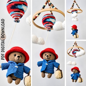 May include: A crochet mobile featuring a bear wearing a red hat and blue coat, holding a beige suitcase, suspended below a red, white, and blue balloon and white clouds. The mobile includes a wooden ring with colorful beads. PDF DIGITAL DOWNLOAD.