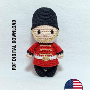 Puede incluir: Una muñeca de ganchillo de un guardia británico con un sombrero negro alto, una túnica roja con bordados dorados, un cinturón blanco y pantalones negros. La muñeca tiene una cara de color beige claro con ojos de cuentas negras. Texto: PDF DIGITAL DOWNLOAD.