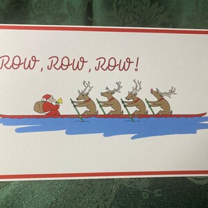 May include: A Christmas card with a red border and white background. The card features a cartoon illustration of Santa Claus in a red suit and hat, rowing a boat with four reindeer. The reindeer are wearing red collars and are rowing with their antlers. The text "ROW, ROW, ROW!" is written in red cursive at the top of the card.